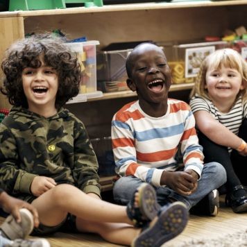 A photo of 3 children sitting on the floor and laughing during a Little Lights workshop.